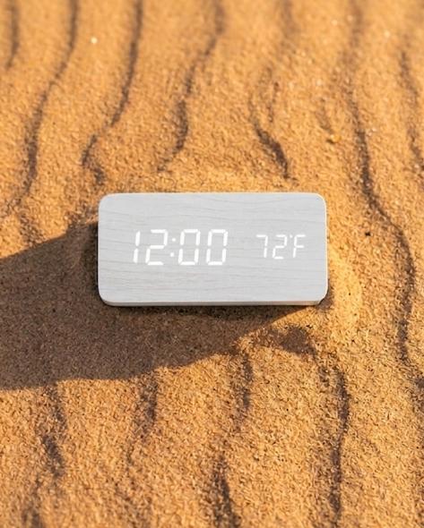 Digital clock displaying time and temperature on sand